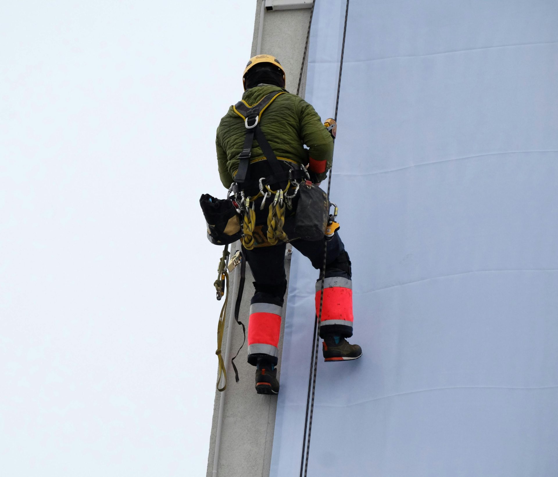 Ein Seilzugangstechniker klettert zur Durchführung von Wartungsarbeiten an der Gebäudefassade empor.